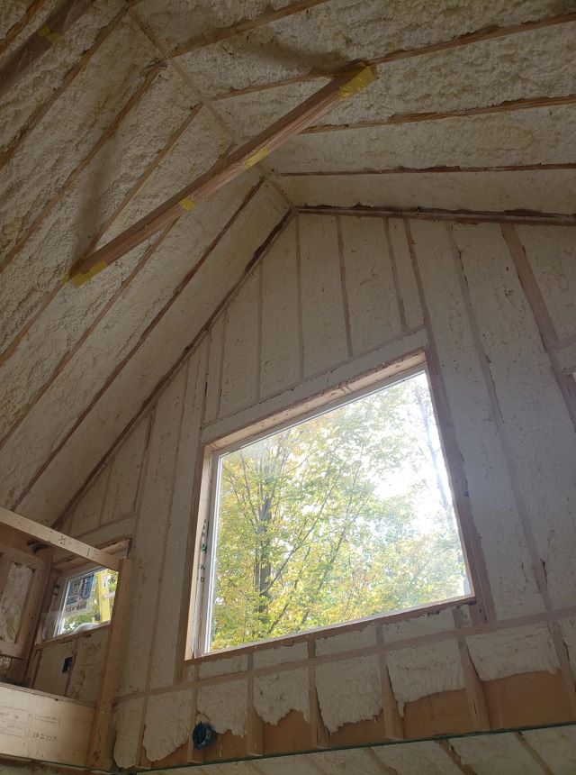 Vaulted room interior with spray foam insulation across the roof deck and walls around a window